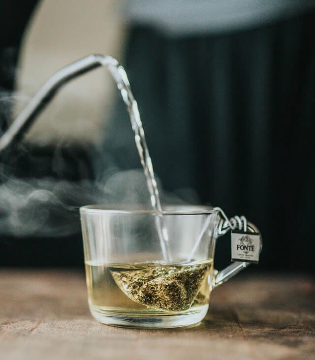 Teebeutel mit grünem Tee wird in einer Tasse mit kochendem Wasser übergossen.